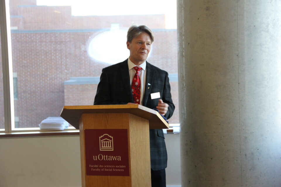 A man in a suit and tie stands at a podium delivery a speech. The podium reads "The University of Ottawa."