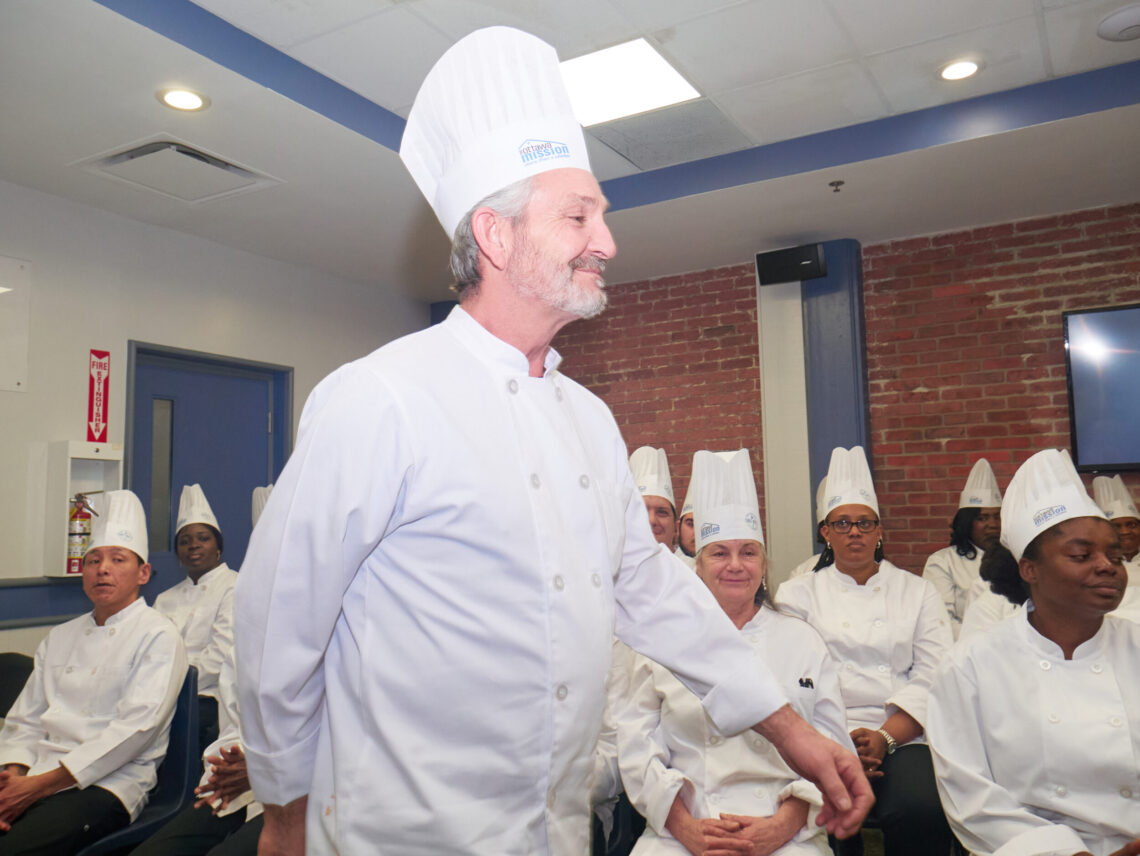 A smiling male chef in full gala uniform walking to the podium during his graduation.