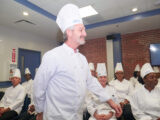 A smiling male chef in full gala uniform walking to the podium during his graduation.