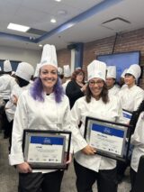 Two smiling female chefs show proudly their certificates.