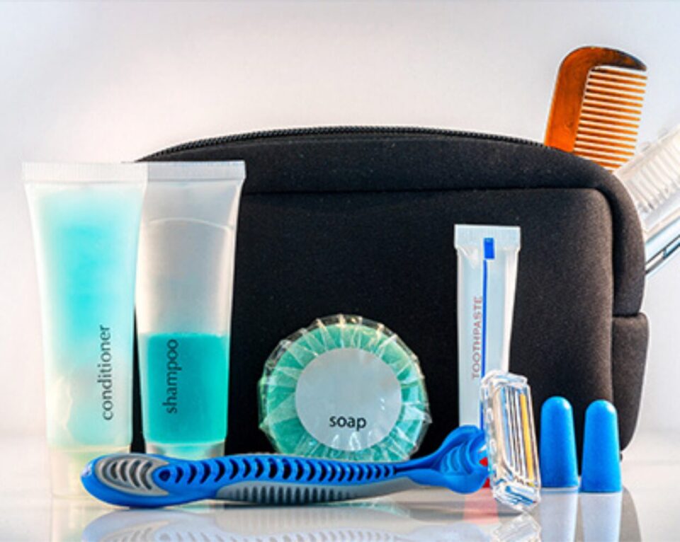 oiletry kit with black bag, includes blue shampoo, conditioner, soap, toothpaste, razor, earplugs, toothbrush, and comb, conveying travel essentials.