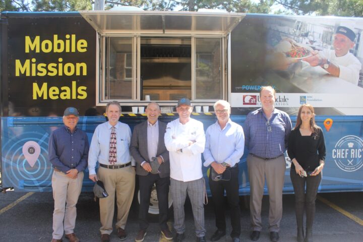5 representatives of Urbandale Corporation pose with Chef Ric in front of the Mobile Mission Meals truck.