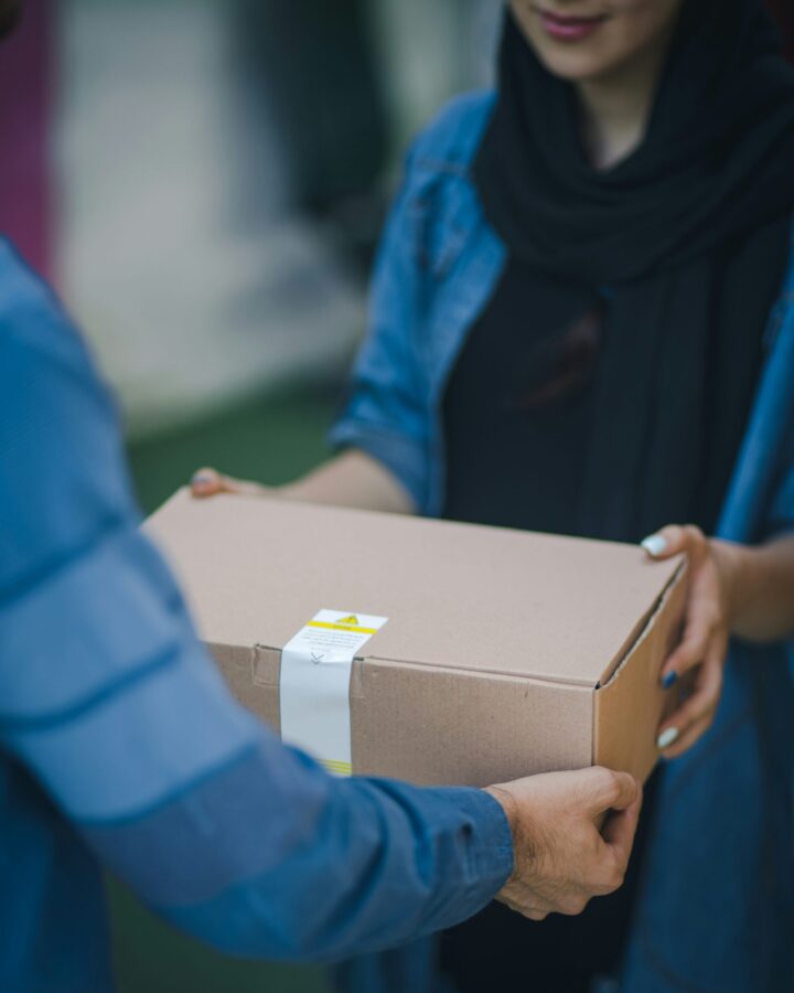 A close-up of two people exchanging a cardboard package. One person hands over the box, while the other receives it.